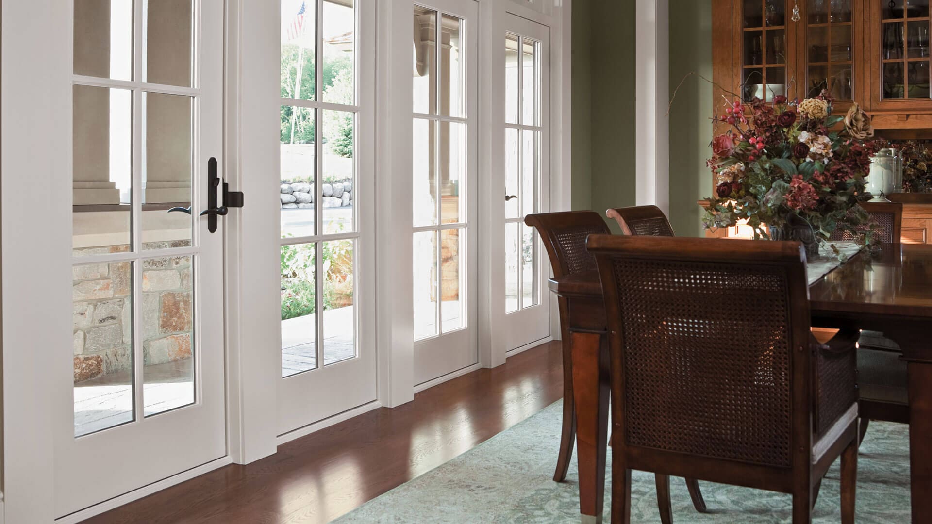 Patio Doors Kenosha WI Dining room with wood flooring, large dining table with three visible chairs, and a pair of Frenchwood patio doors leading outside.