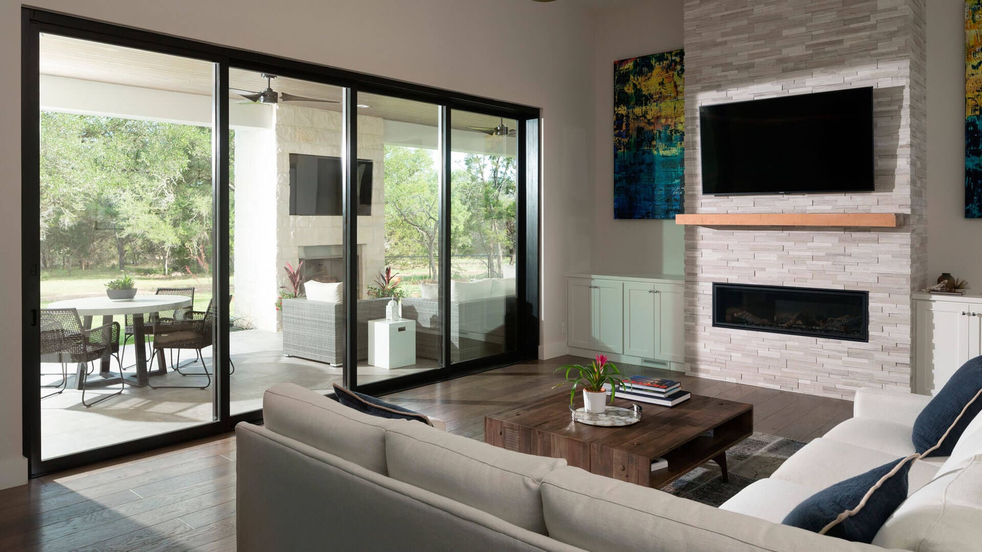 Modern living room with wood flooring, flatscreen tv, and large sliding patio doors leading to outdoor living area.